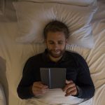 Handsome young man using a digital tablet while lying in bed. Reading in bed, using kindle, top view.
